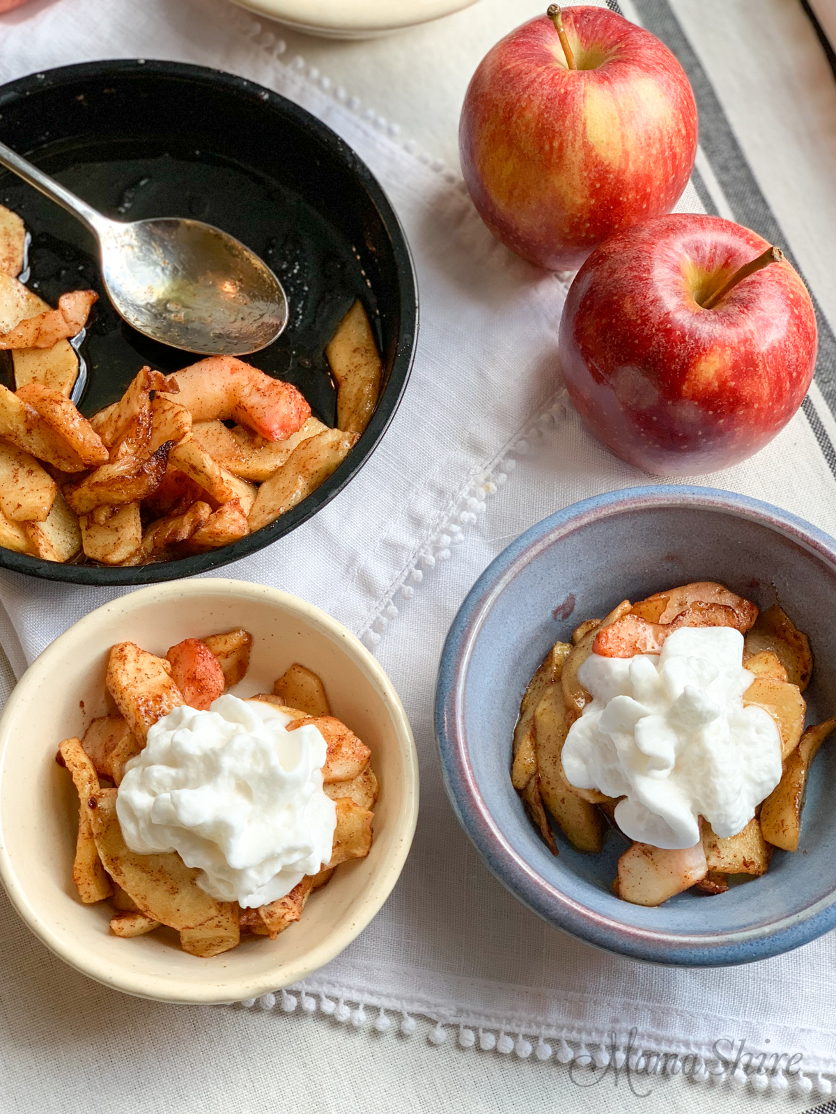 Two red apples and two serving dishes of sliced spiced apples with whipped topping on top. Yummy Air-Fried Spicy Apples