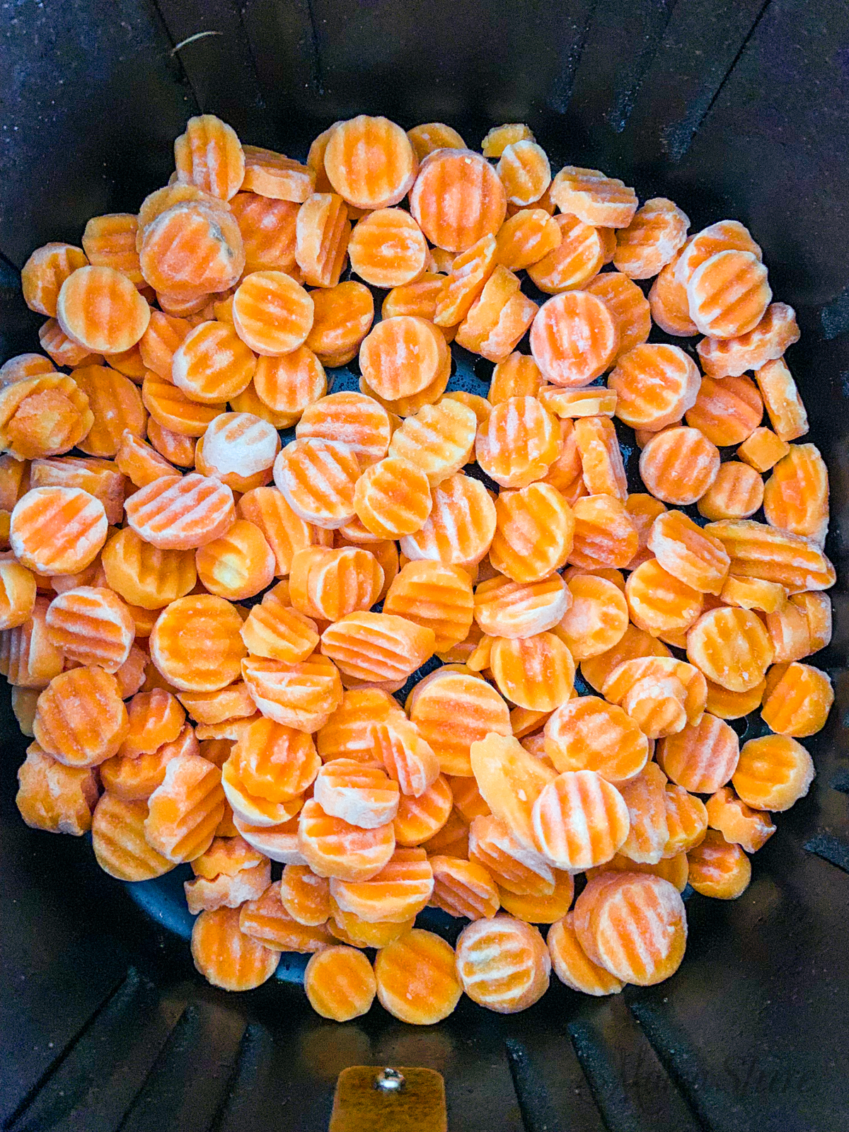 Frozen carrots in an air fryer basket.