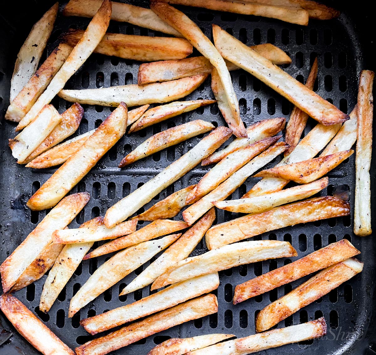 An air fryer basket with freshly fried french fries.