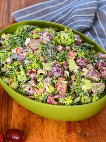 A green serving bowl filled with delicious broccoli salad with grapes and bacon.