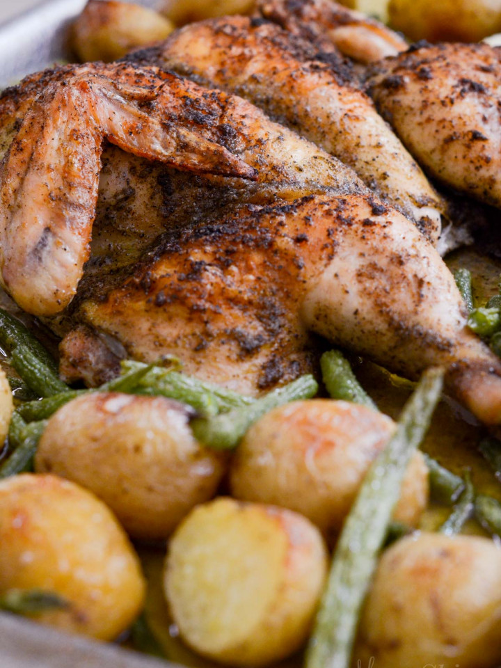 A side view of a roasted chicken that has been butterflied with potatoes and green beans.
