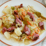 A white dinner plate with a serving of gluten-free cabbage and sausage .