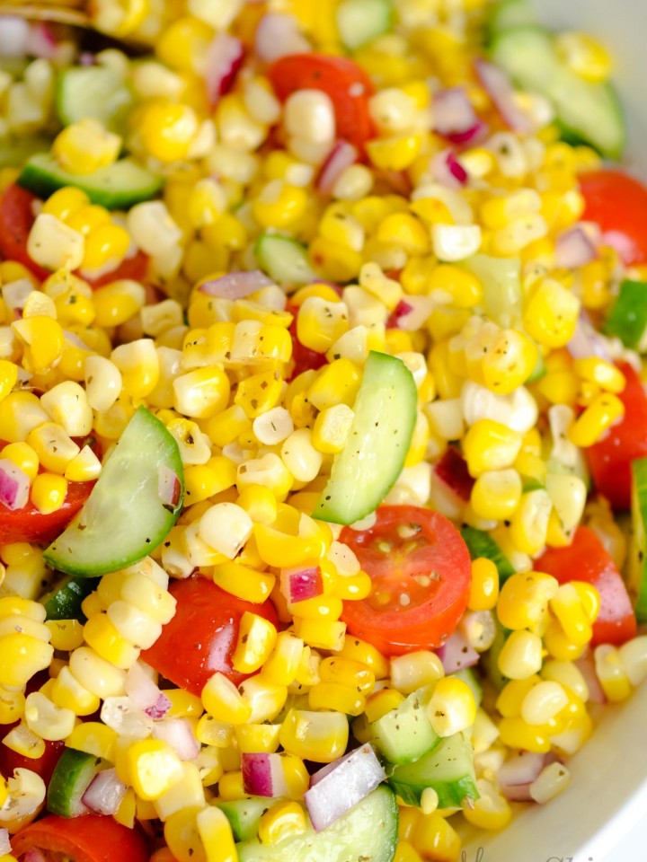 A closeup of a corn, cucumber, tomato, and red onion salad