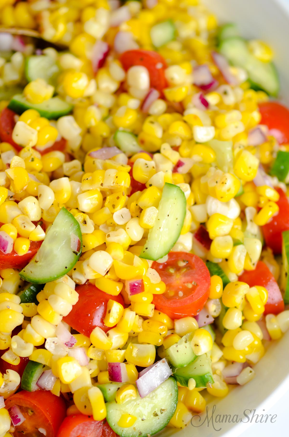 A closeup of a corn, cucumber, tomato, and red onion salad