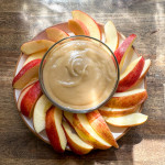 A bowl of dairy-free caramel dip surrounded by apple slices.