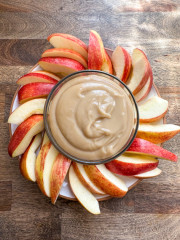 A plate of sliced apples with a bowl of dairy-free caramel dip in a small bowl in the center.