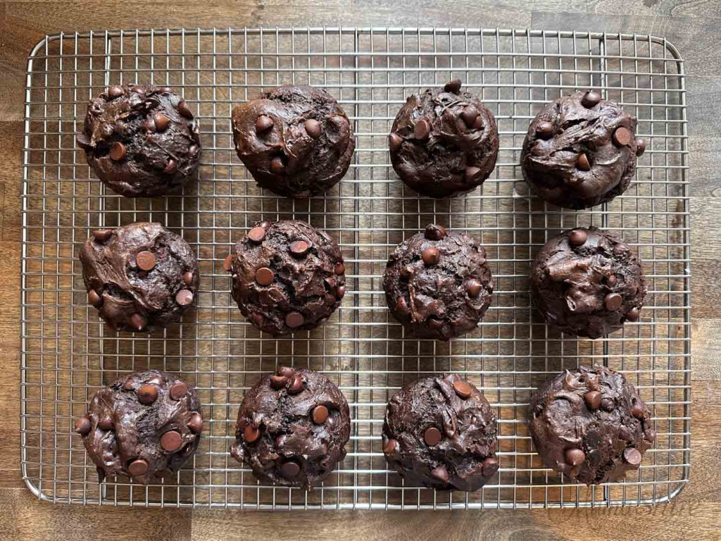 A dozen chocolate muffins that have been baked and are cooling on a wire rack.