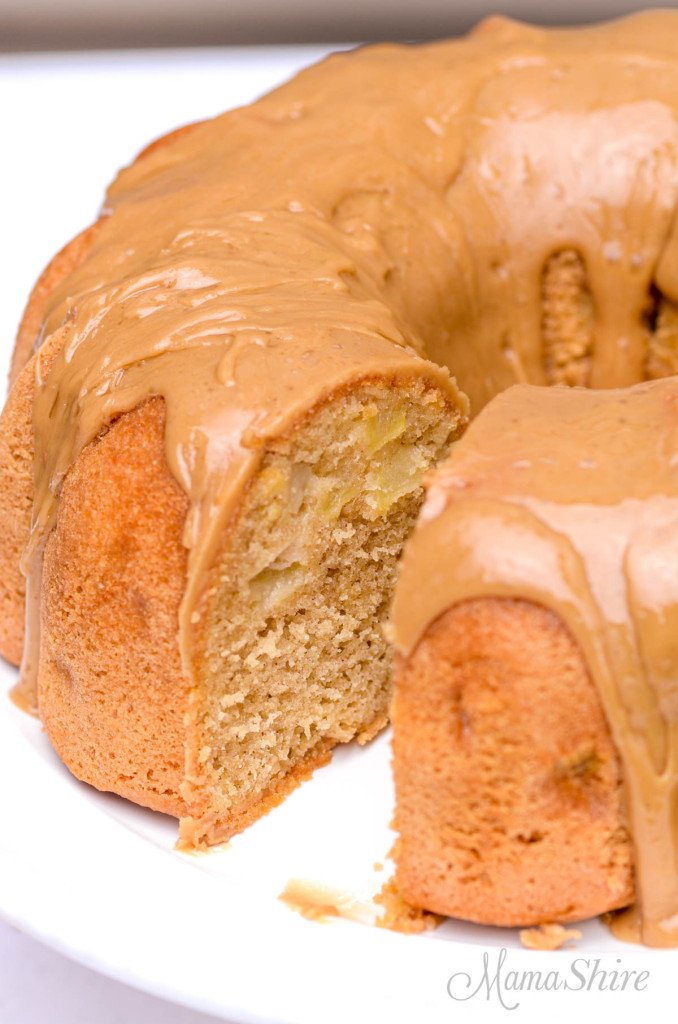 An apple bundt cake with caramel icing and one slice removed.