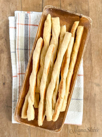 A wooden platter filled with long gluten-free breadsticks.