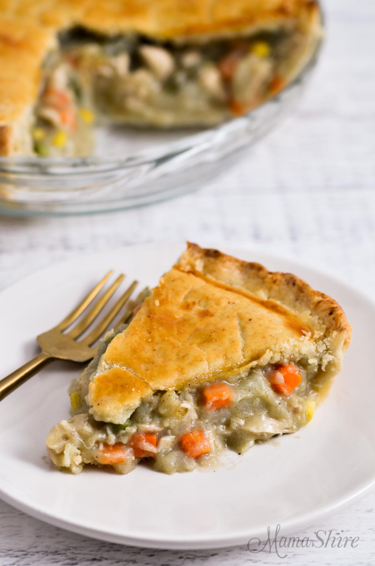 A slice of chicken pot pie on a plate with the rest of the pie in the background.