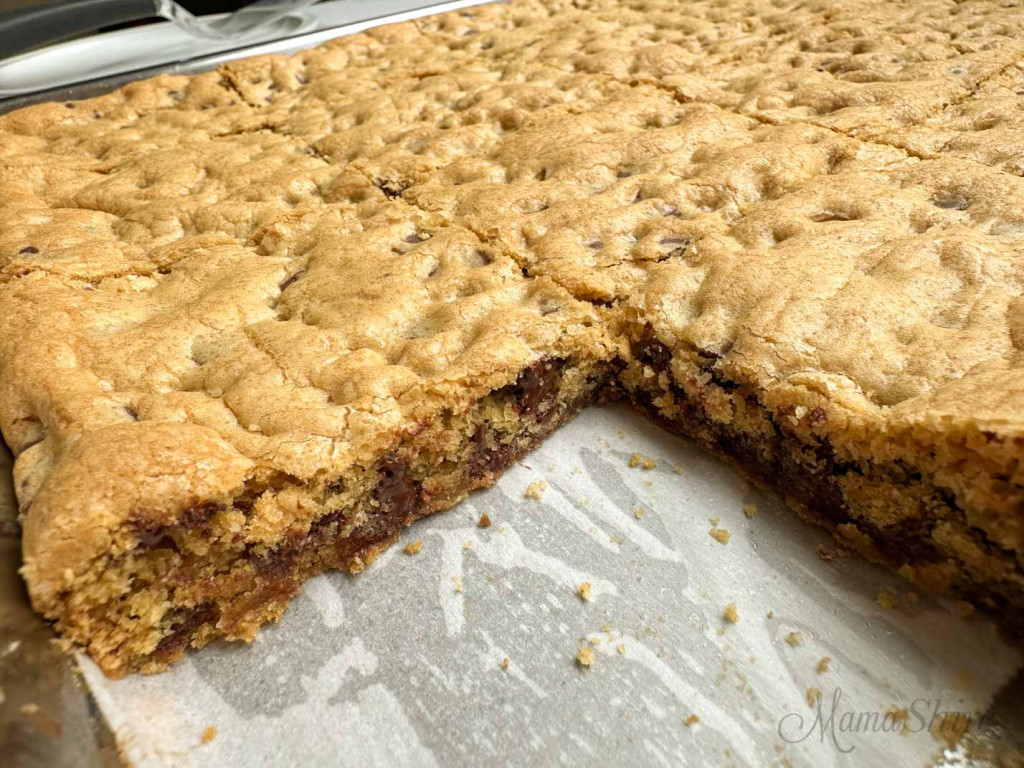 Chewy chocolate chip cookie bars in a the pan with one bar cut out. 