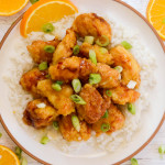 A serving of gluten-free orange chicken on top of white rice with a sprinkling of sliced green onions.