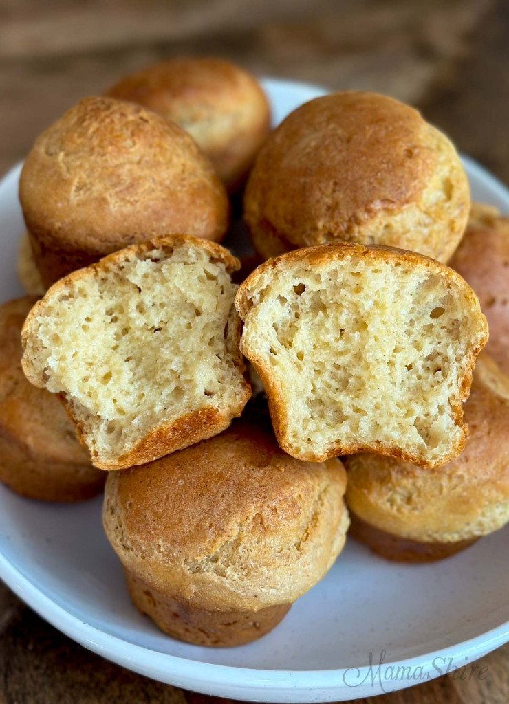 Yummy gluten-free rolls in a serving dish with the top roll pulled into so you can see the tender crumb on the inside. 