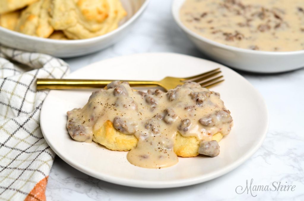 Gluten-free and dairy-free sausage gravy poured over two gluten-free biscuits. With more gravy in a bowl in the background.