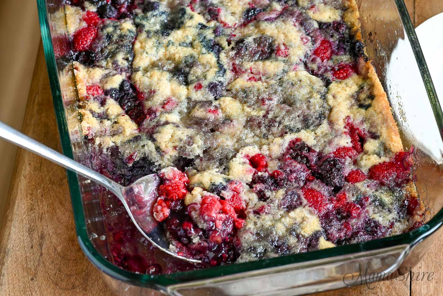 Freshly baked gluten-free cobbler with a serving being removed with a large spoon.