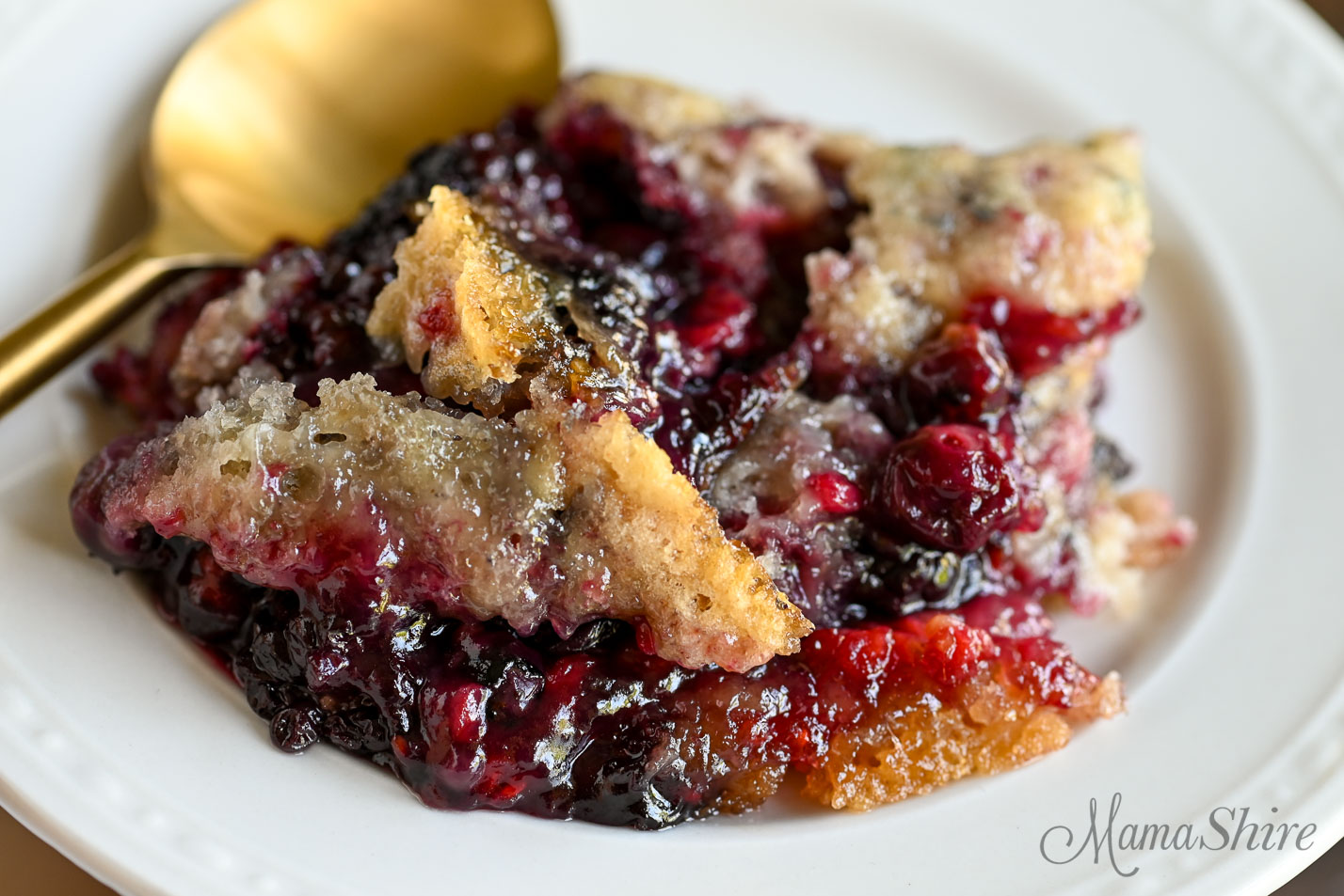 A close up pic of a serving of gluten-free triple berry cobbler on a white serving plate.