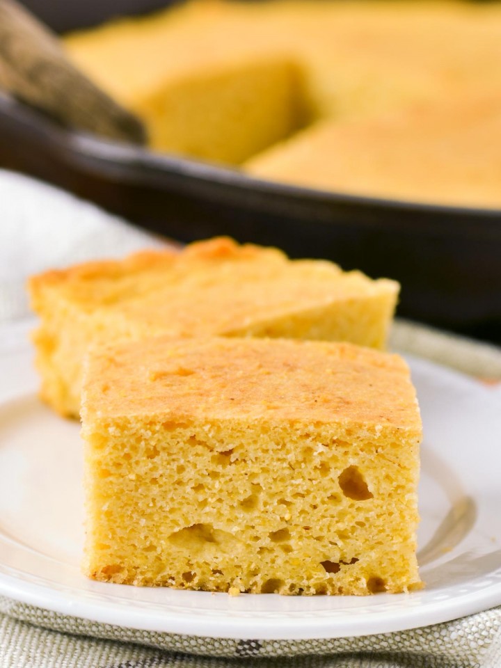 Gluten-free cornbread on a white serving plate with a cast-iron skillet of cornbread in the background.