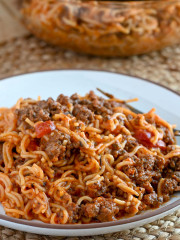 A serving of spaghetti on a white plate with a serving bowl in the background.