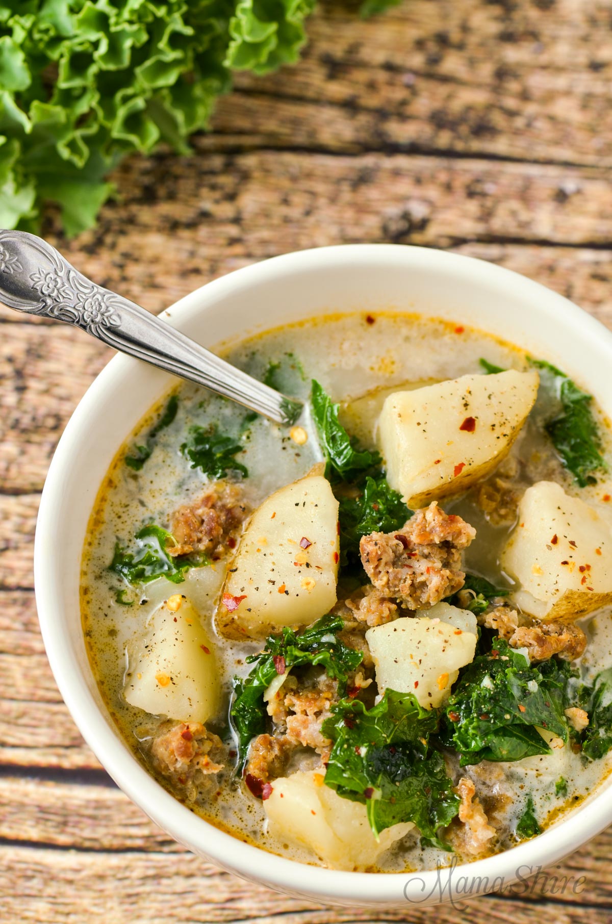 A white bowl with dairy-free soup that has potatoes, kale, and sausage.