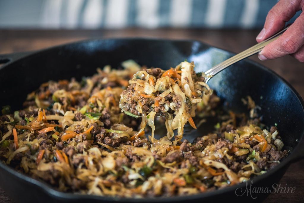 Mongolian beef egg roll in a bowl in a skillet with a spoonful of it lifted up.