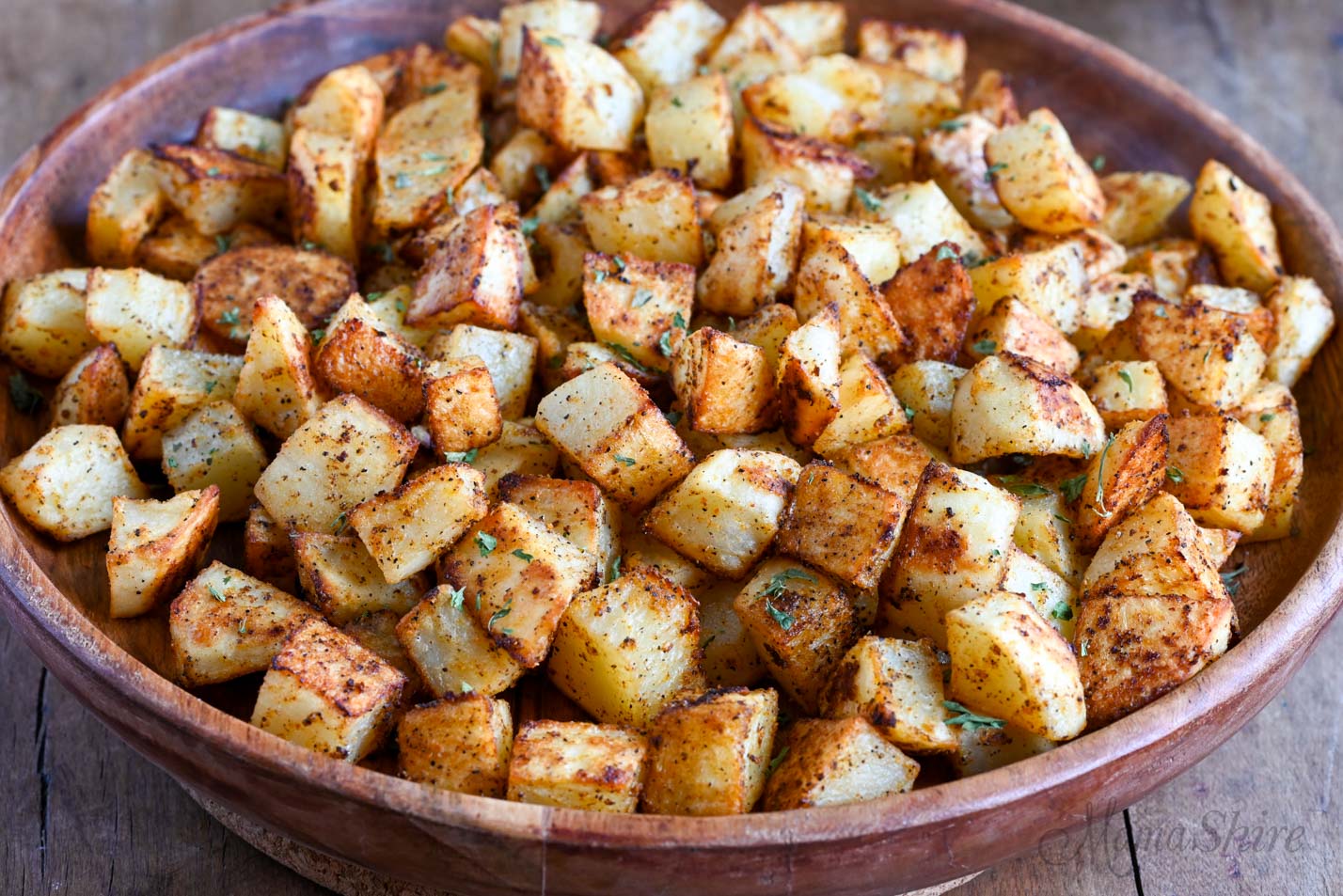 A wooden serving bowl with crispy roasted potatoes.