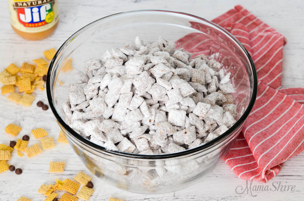 A big party bowl of puppy chow with some rice chex and chocolate chips scattered about.