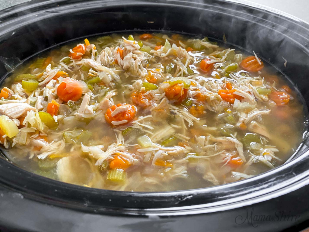 Steam rising up from the slow cooker that's full of chicken soup.