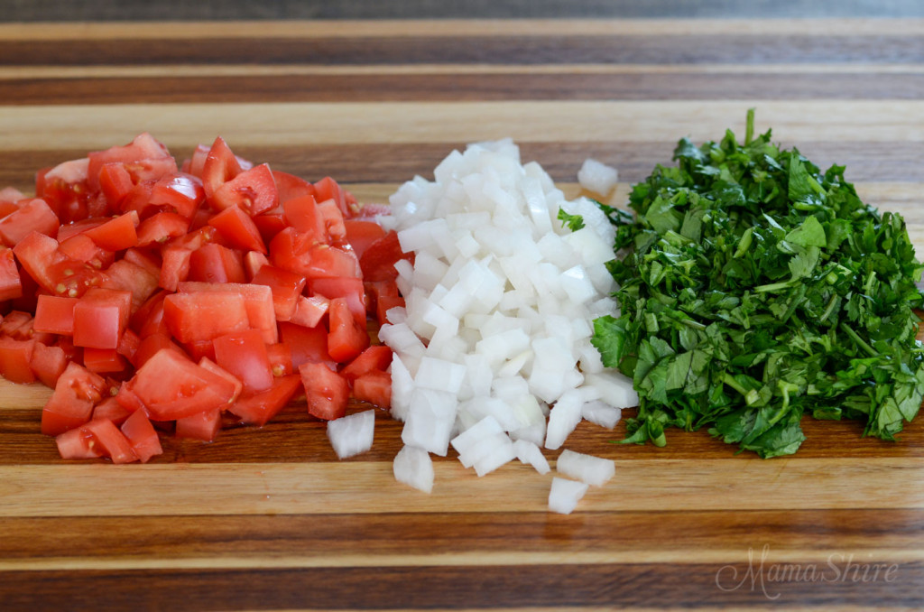A wooden cutting board with chopped tomatoes, white onion, and cilantro that will be going into a homemade restaurant-style salsa.