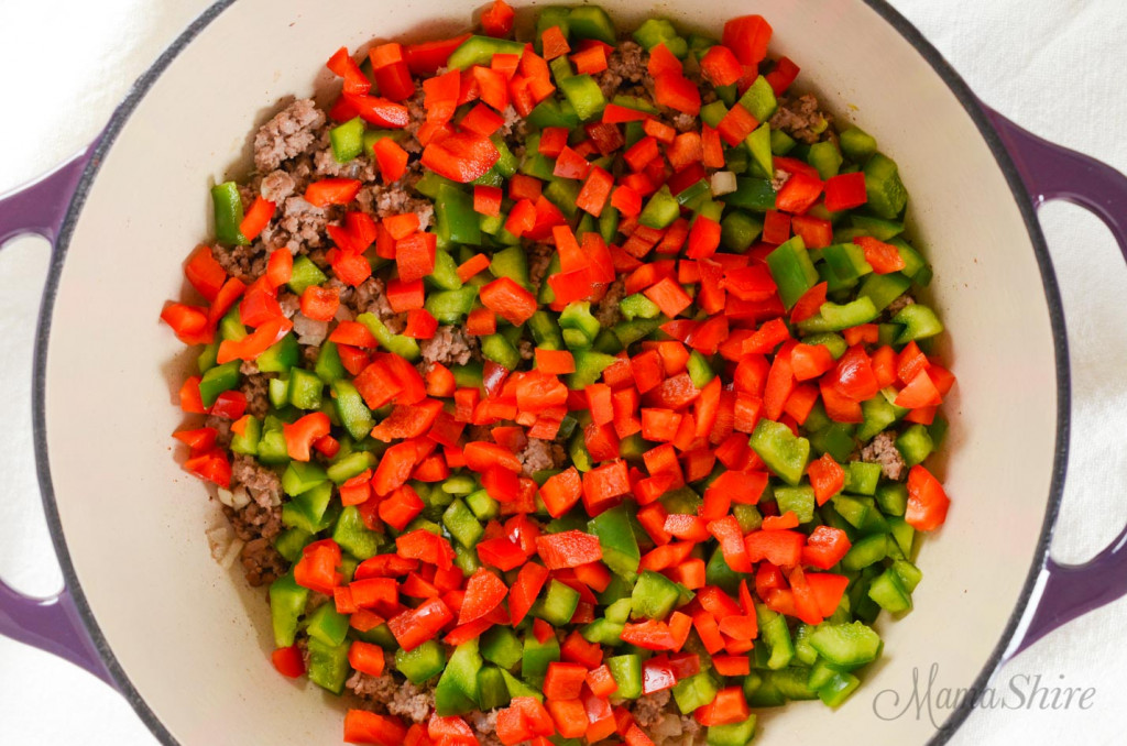 Red and green bell pepper on top of browned beef for a stuffed bell pepper soup.