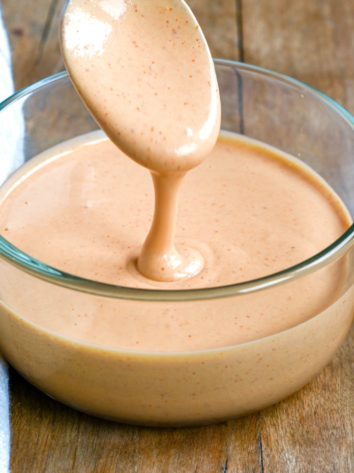 Homemade yum yum sauce in a glass bowl with some it being drizzled from a spoon.